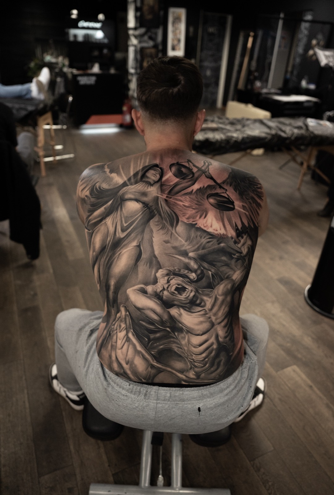 Black and grey full back tattoo with scales of justice and mythic figures