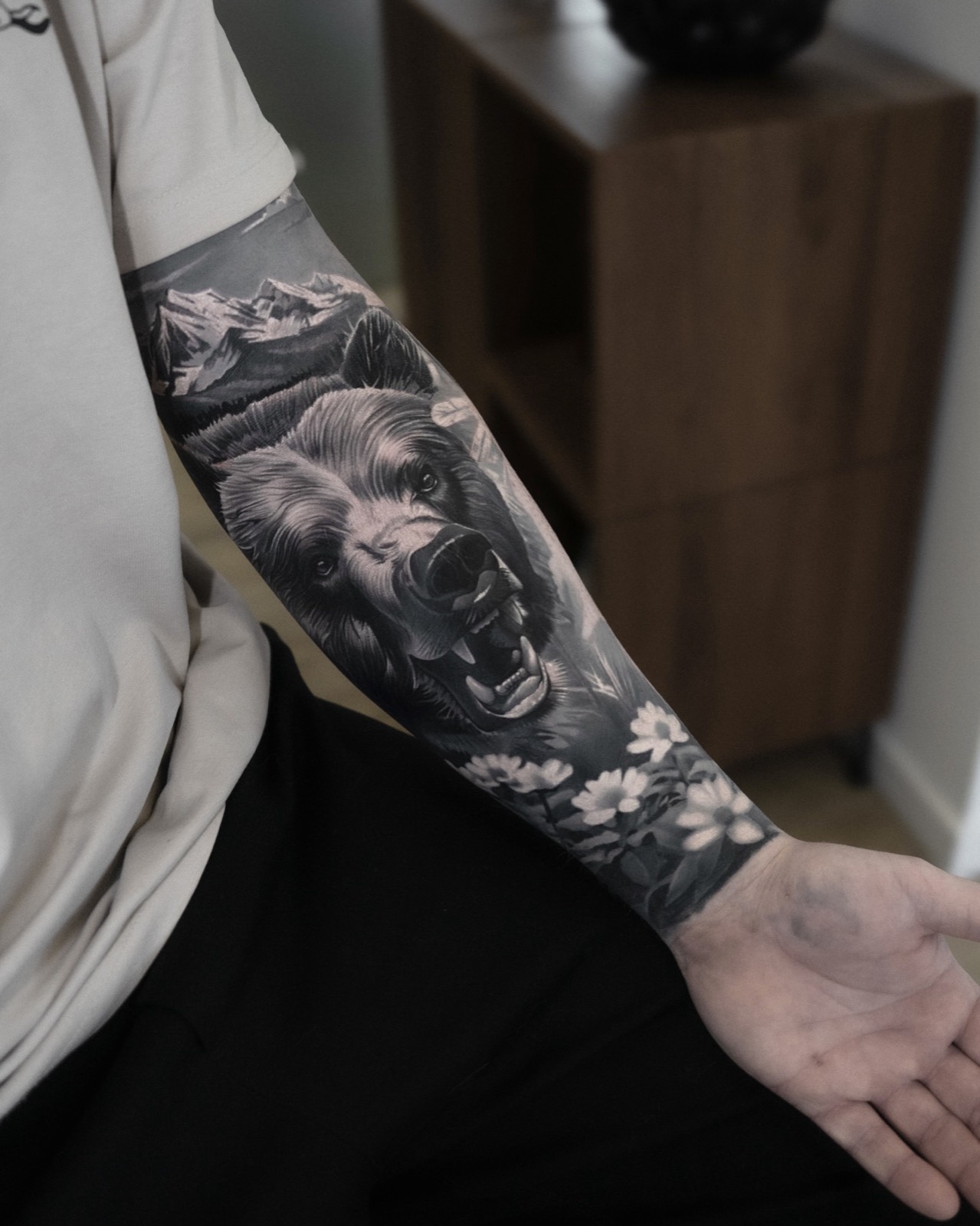 Realistic black and grey bear forearm tattoo with mountain scenery